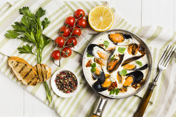 Flat-lay mussels in white sauce and sides on tablecloth