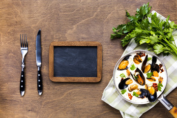 Flat-lay mussels in white sauce on tablecloth with blackboard