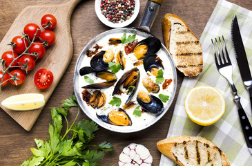 Flat-lay mussels in white sauce with tablecloth and cutlery
