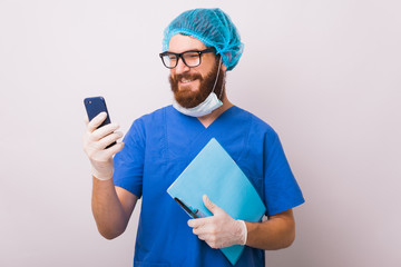 Smiling doctor looking at smartphone and holding some paper work