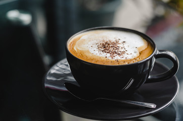 close up modern hot black coffee the cappuccino on dark background with coffee bubble foam pattern and texture in black cup looking and feel so delicious on glasses table in coffee shop.