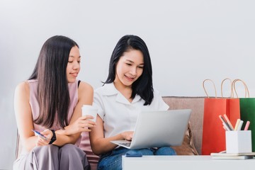 Asian beautiful woman and friend using laptop with credit card shopping online together at home with shopping bag and laptop.Convenience buying online products with business technology concept.