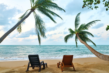 Tropical landscape with two sun loungers under palm tree leaves and sea view