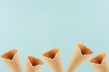 Summer food decorative border of empty waffle ice cream cones on soft light green background, copy space.
