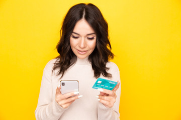 Woman using phone and credit card isolated at the yellow background