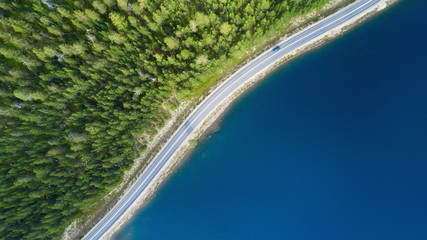 Beautiful aerial view of road between green summer forest and blue lake in Lapland. Car moving on...