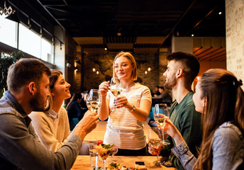 Group of young friends having fun in restaurant, talking and laughing while dining at table.