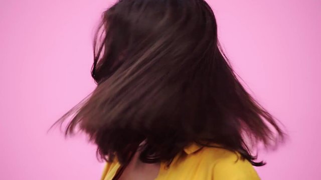 slow motion of beautiful girl shaking head, looking at camera and smiling Isolated On pink