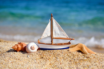 Toy ship and seashells on sand near sea. Summer vacation concept