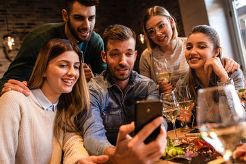 Group of young friends having fun in restaurant, talking and laughing while dining at table.