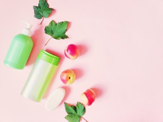 Fototapeta na wymiar Herbal bath products for hair and skin care. Green shampoo bottle, organic shower gel, soap bar, currant leaves and nectarines on a pink background. Flat lay beauty photo