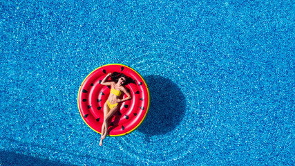 Aerial top view of woman wearing a hat sitting in inflatable watermelon in calm waters of a pool