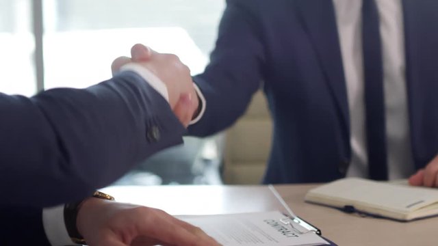 Mid-section PAN shot of unrecognizable businessman in suit writing notes in notebook, then shaking hands with male executive and leaving conference room after signing partnership contract
