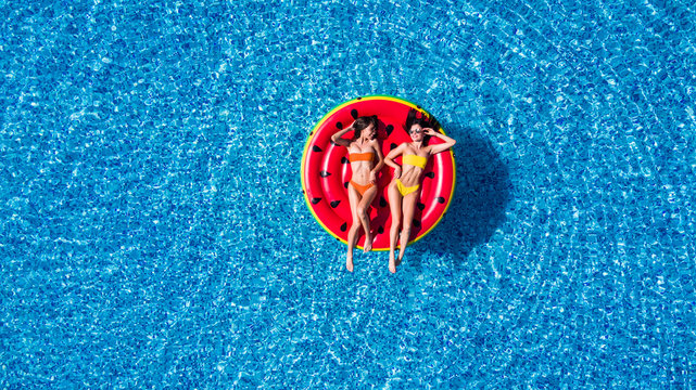 Aerial view of two women lying on inflatable watermelon mattrass floating and relaxing in pool
