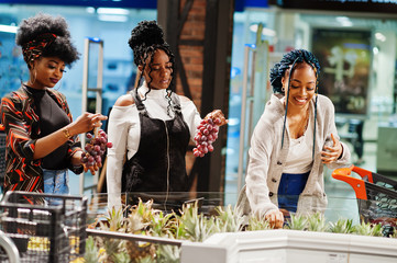 Group of african womans with shopping cart buying exotic fruits in grocery store supermarket.