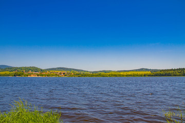 The Lipno Dam - Horni Plana, Czech Republic, in a bright summer day. The lake is calm, has clean blue water. There are no clouds in the sky. Lot of trees on the background.