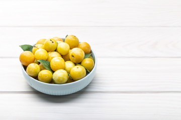 Yellow plum mirabelle fruit in bowl on white wooden table. Copy space
