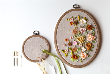 Handmade embroidery satin ribbons with flowers ornament on linen canvas in plastic hoop and special needles with a big eyelet (embroidery made by the author of the photo). Copy space, flat lay © Katvic