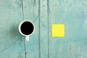 Coffee cup and yellow sticky note on green wooden desk