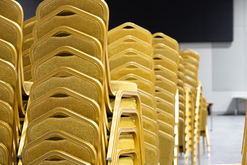Stack Steel Chair Fabric seat pad yellow gold color and Table arrange in row ready to set up for big meeting, conference, business, workshop, gala dinner, Wedding ceremony in Convention Hall of Hotel