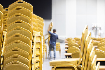 Stack Steel Chair Fabric seat pad yellow gold color and Table arrange in row ready to set up for big meeting, conference, business, workshop, gala dinner, Wedding ceremony in Convention Hall of Hotel