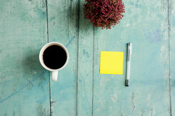 Sticky note and pen on green wooden table with plant and coffee
