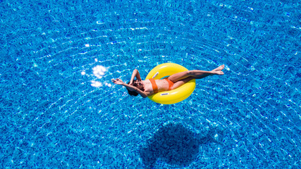 Beautiful woman relaxing on inflatable ring in blue swimming pool.
