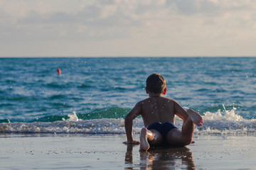 The boy lies on the edge of the pier near the sea. A boy is playing with big waves and big splashes on the pier. Sunset, closeup, selective focus