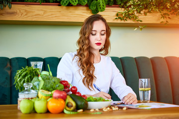 Obraz na płótnie Canvas Woman dietitian in medical uniform with tape measure working on a diet plan sitting with different healthy food ingredients in the green office on background. Weight loss and right nutrition concept