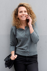 middle age woman smiling and talking with mobile phone by gray background