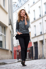 Obraz premium Full length attractive woman walking on street and talking with mobile phone