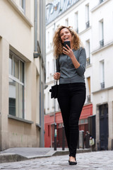 Full length attractive woman walking on city street with mobile phone