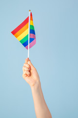 Closeup of a hand waving a small rainbow flag against a light blue background