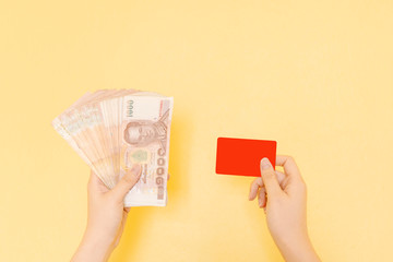 home business and job success concept from beauty hand of woman hold and show lot of banknote on left hand and credit card on right hand with yellow pastel background