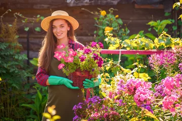 Foto op Canvas Portrait of happy joyful florist gardener woman in hat with flower pot of petunia in home garden. Gardening and floriculture © Goffkein