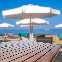 Wooden table background with sun beds and umbrellas on the beach and ocean view.