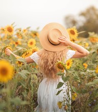 Beautiful curly young woman in a sunflower field holding a wicker hat. Portrait of a young woman in the sun. Summer.