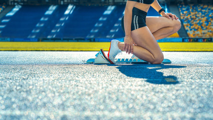Side view cropped shot of female runner sitting at the start line on running track