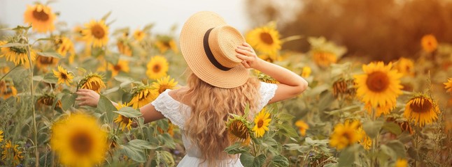 Beautiful curly young woman in a sunflower field holding a wicker hat. Portrait of a young woman in...