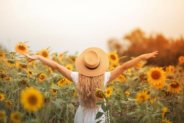 Beautiful curly young woman in a sunflower field holding a wicker hat. Portrait of a young woman in the sun. Summer.