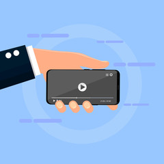 The hand holds the phone with an open video on the screen on a blue background.