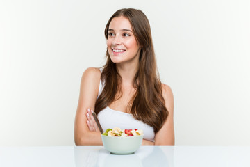 Young caucasian woman eating fruit bowl smiling confident with crossed arms.