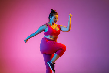 Young caucasian plus size female model's doing exercises on gradient purple background in neon light. Cardio training, jumping. Concept of sport, healthy lifestyle, body positive, equality.