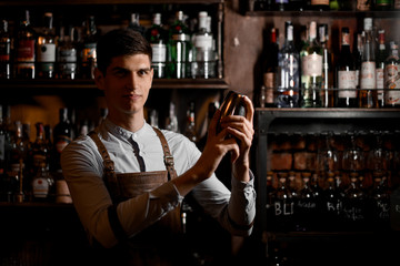 Portrait of young bartender in apron preparing cocktail