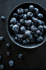 Fresh blueberries in a dark ceramic bowl on a black background, top view, close-up
