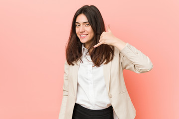 Young brunette business woman against a pink background showing a mobile phone call gesture with fingers.