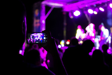 Fototapeta na wymiar The viewer shoots a concert on a smartphone. Bright scene with lights. The focus is blurred