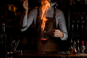 Bartender holds burning sugar above alcohol drink