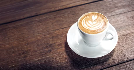 Foto op Plexiglas Close-up van warme cappuccino witte koffiekopje met hartvorm latte art op donkerbruine oude houten tafel in café, eten en drinken concept. © weedezign