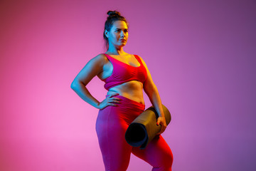 Young caucasian plus size female model's doing exercises on gradient purple background in neon...